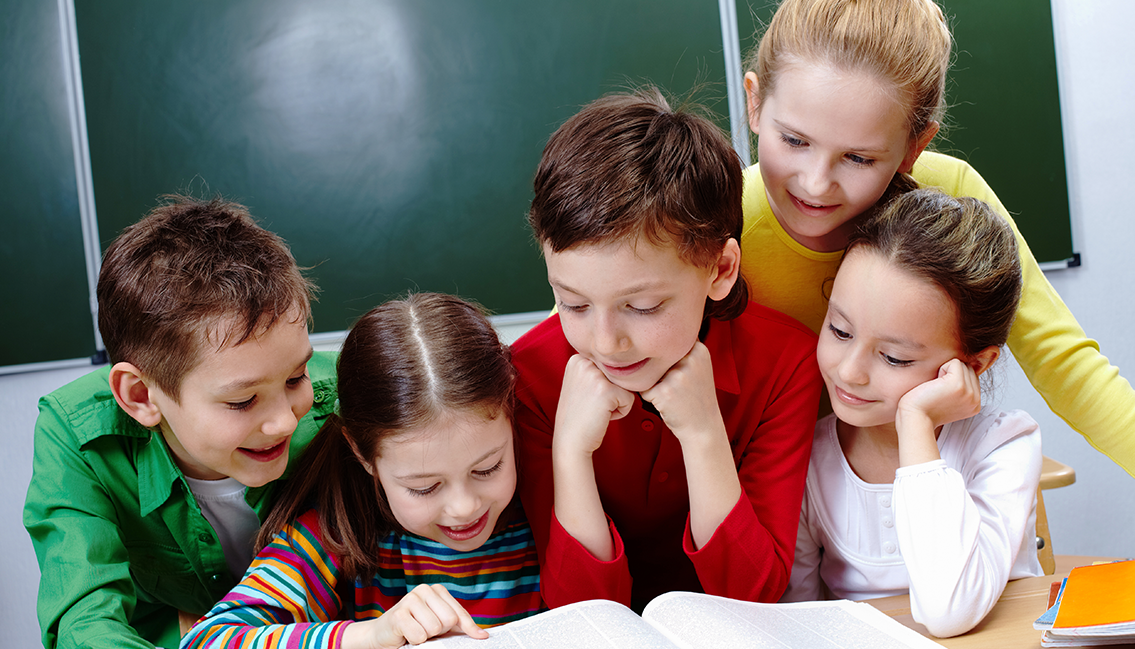 Teacher and a group of young students reading a book together